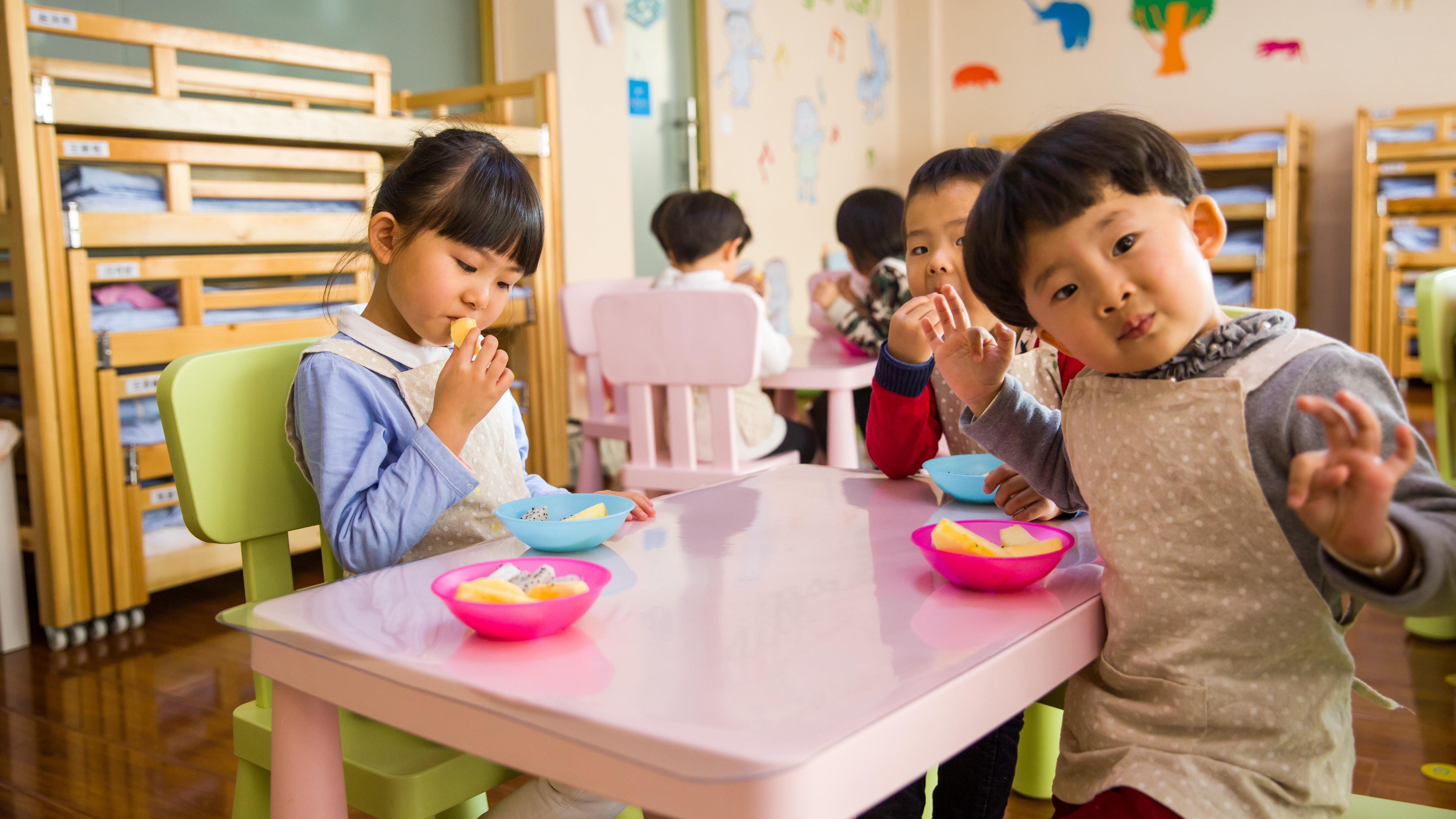 Förskolebarn i Japan äter frukt, sittandes på färgglada möbler. 